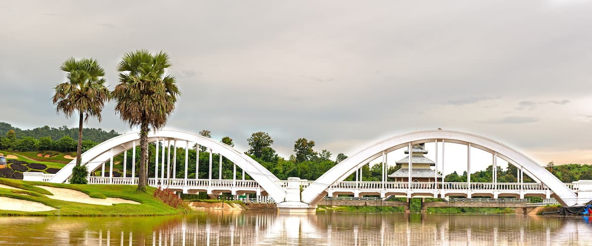 A white bridge with a pagoda-like structure on top, palm trees, and a red train on the tracks.