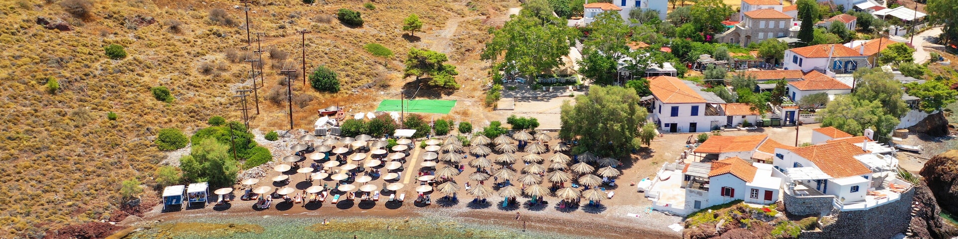 Un pueblo costero con aguas turquesas cristalinas, casas blancas con tejados rojos y una playa con sombrillas.