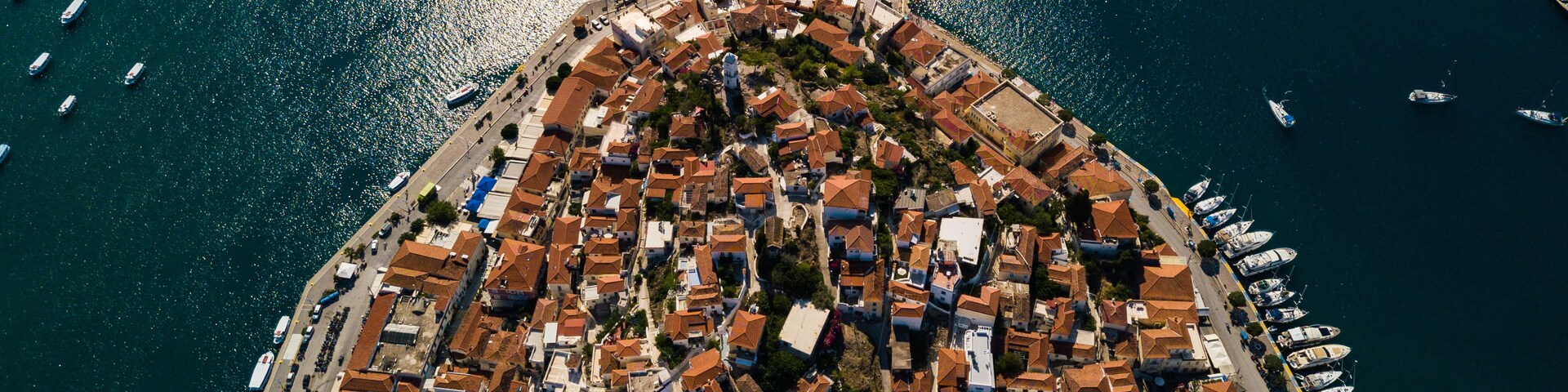 Vista aérea de un pueblo costero con un denso conjunto de edificios, un puerto deportivo con numerosos barcos y una vista despejada del mar.