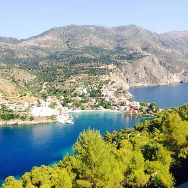 A coastal town nestled between hills, with a clear blue sea and lush greenery.