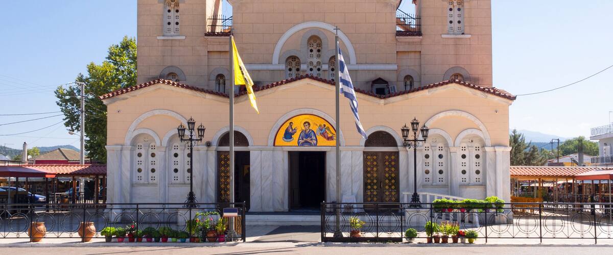 A church with two bell towers, a yellow flag, and a mural of two figures.