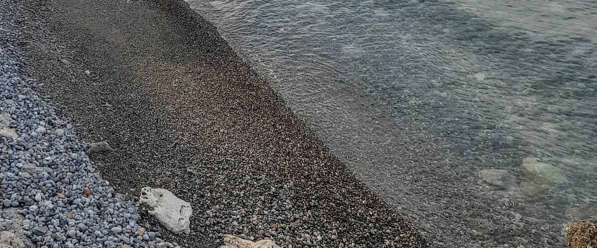 A pebbled beach with a rocky shoreline and calm water.