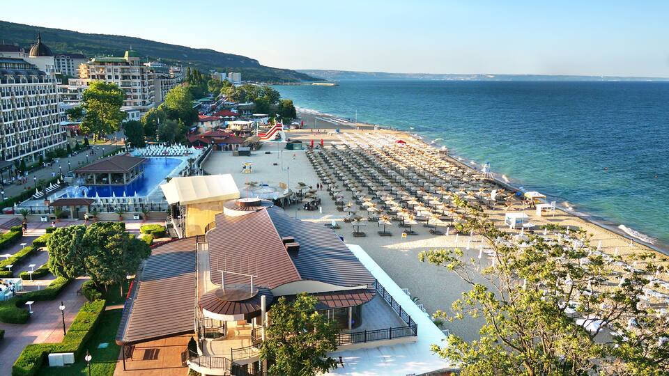 A coastal resort with a beach, pool, and hotel buildings.