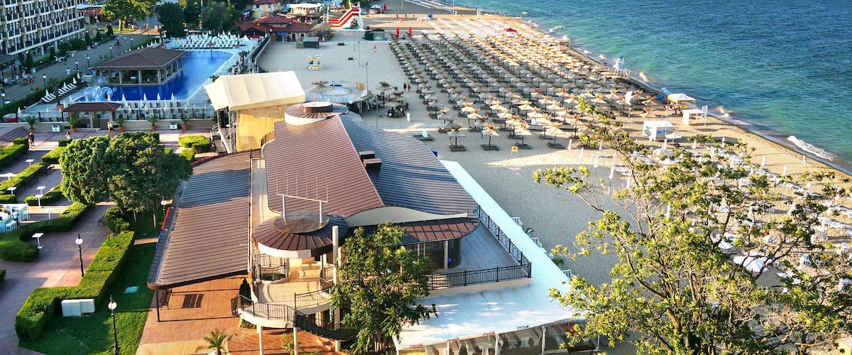A coastal resort with a beach, pool, and hotel buildings.