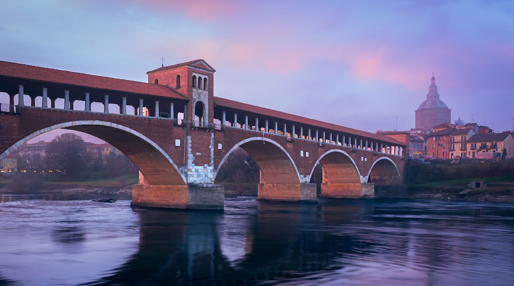 Un puente con varios arcos sobre un río, con edificios y una cúpula al fondo.