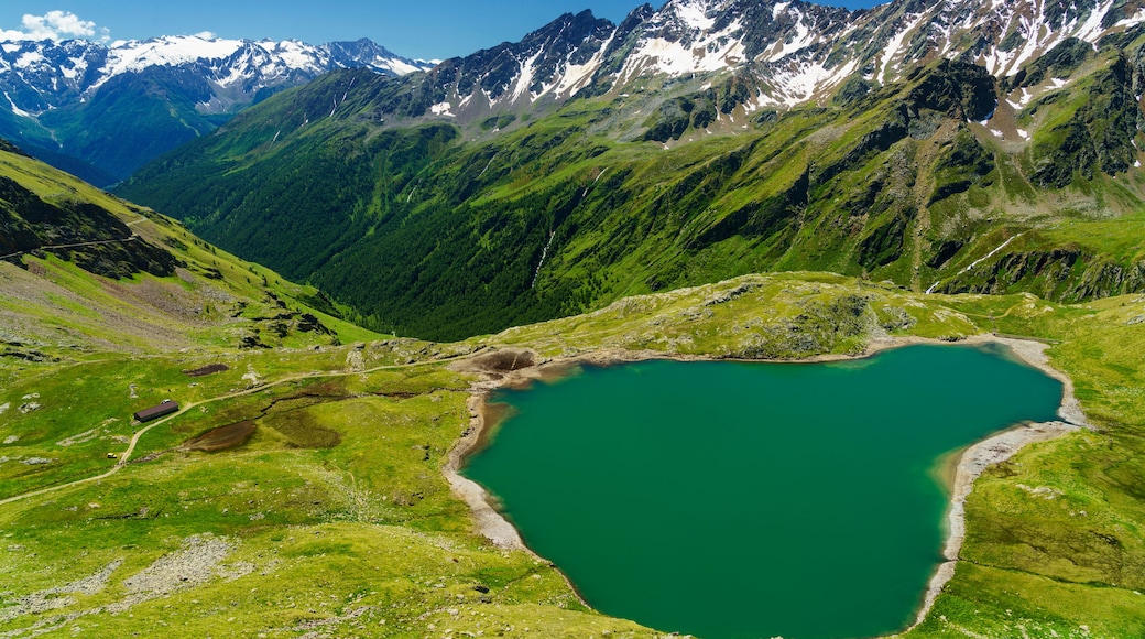 Berglandschap met een turquoise meer, omgeven door groene heuvels en besneeuwde toppen.