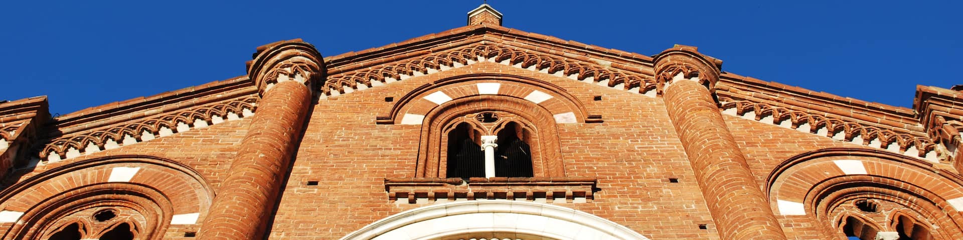 A large brick building with a prominent arched entrance and a clear blue sky above.