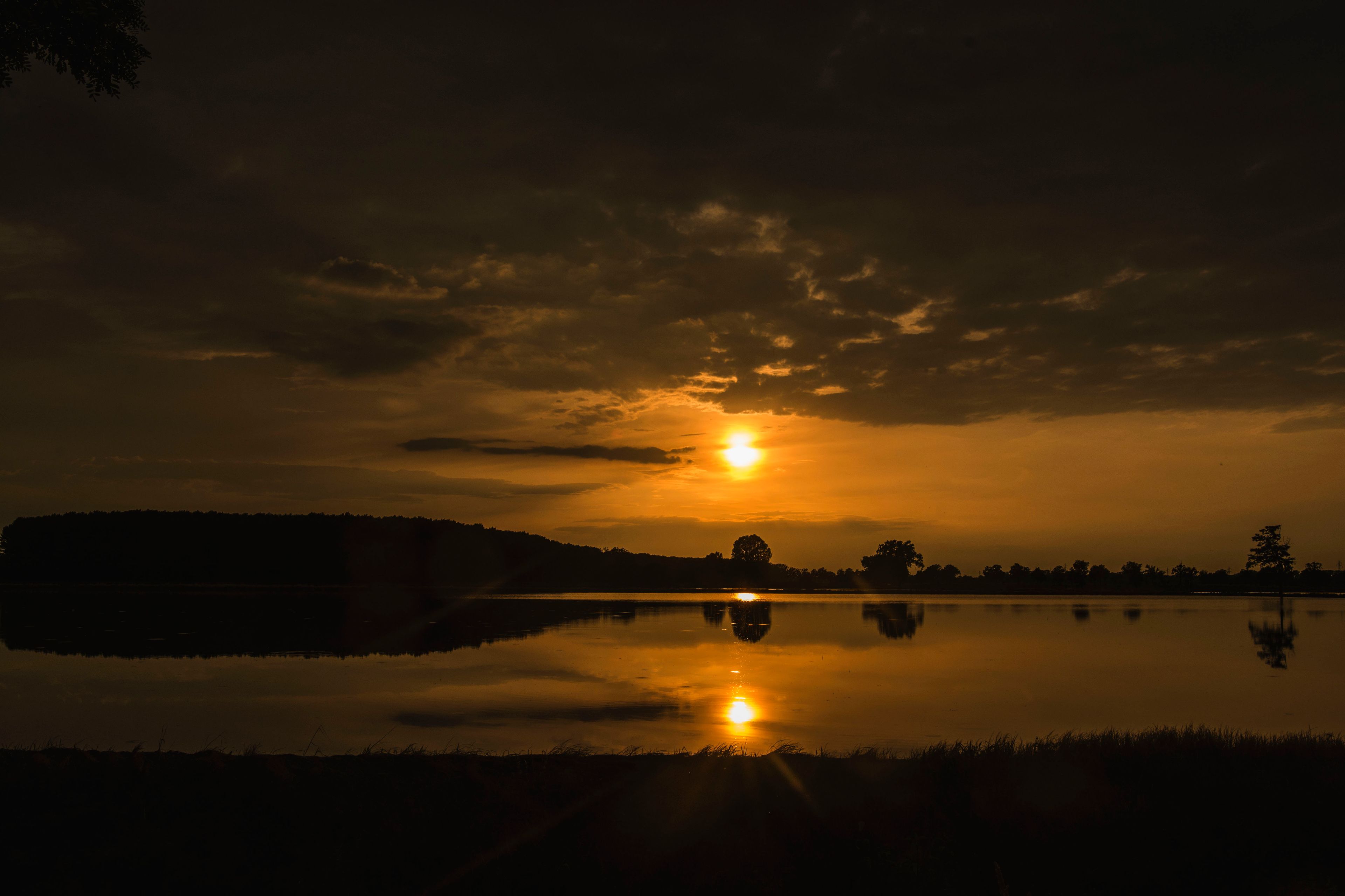 Un atardecer sobre un lago tranquilo con la silueta de una colina a lo lejos.