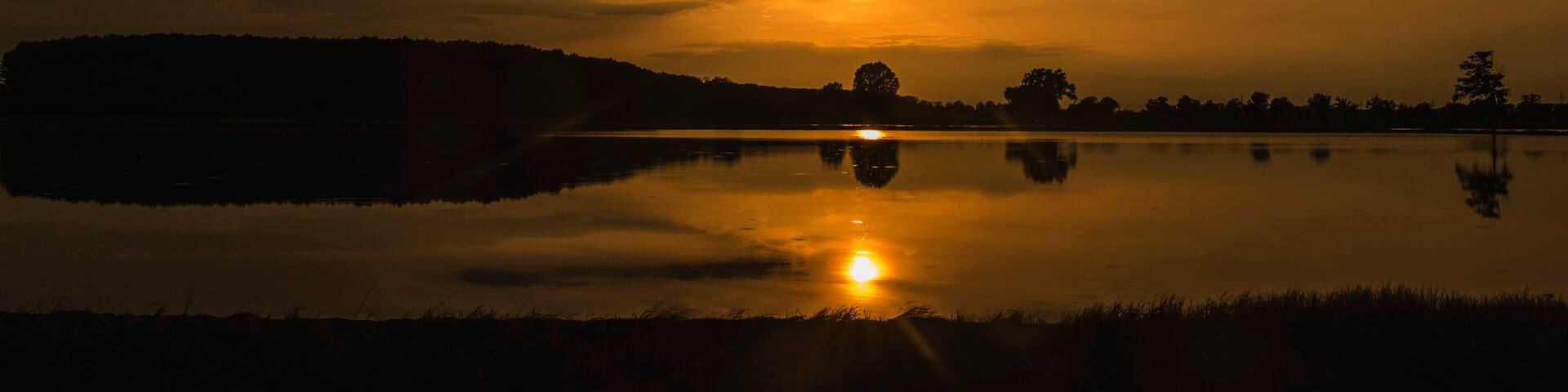 A sunset over a calm lake with a silhouette of a hill in the distance.
