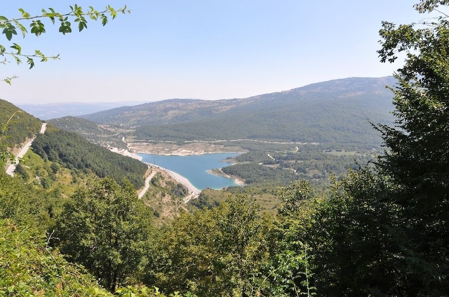 Un lago rodeado de colinas boscosas y una carretera sinuosa.