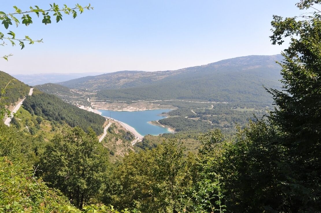 A lake surrounded by forested hills and a winding road.
