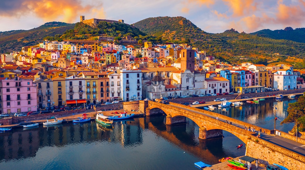 A coastal town with colorful buildings, a bridge over water, and hills in the background.