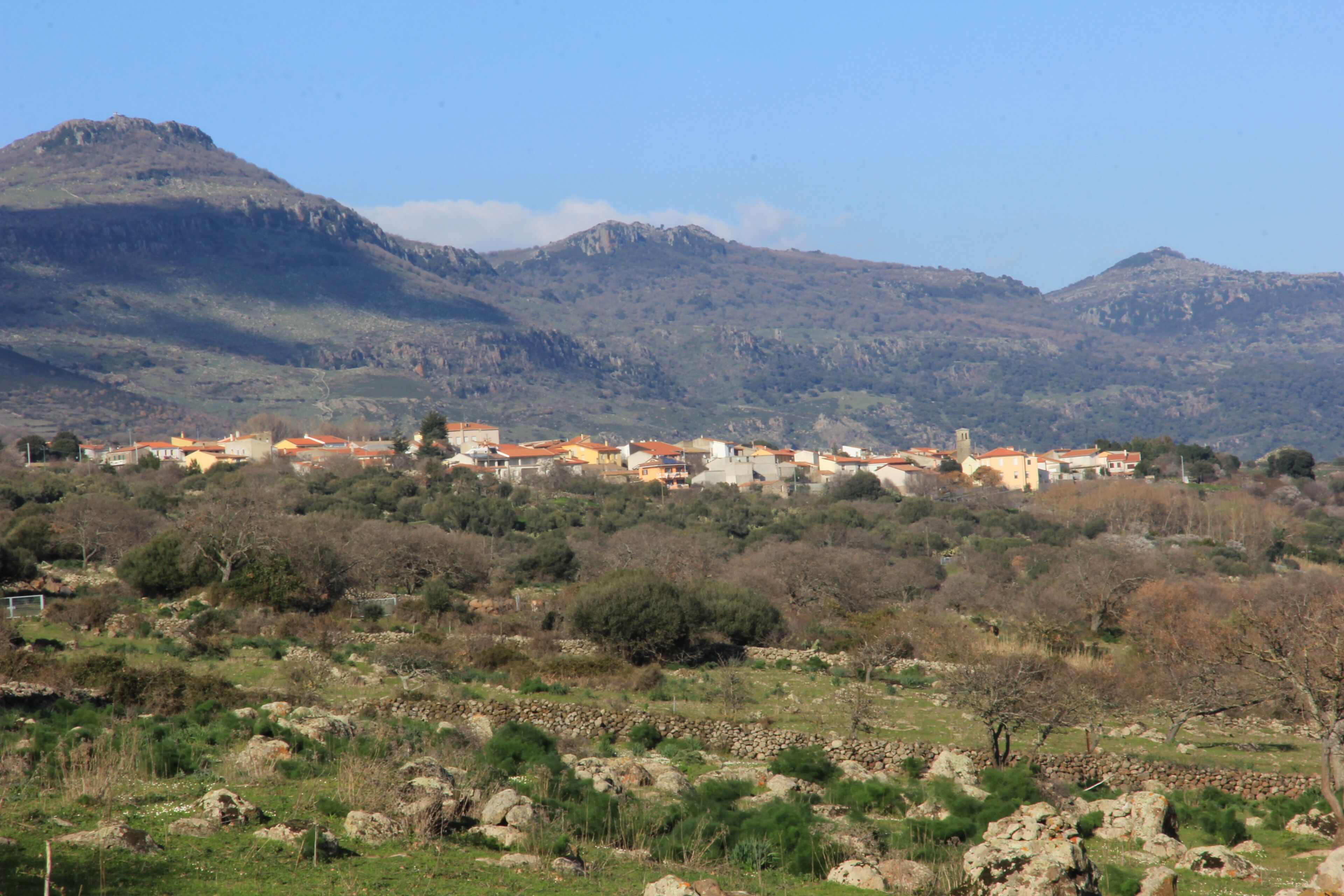 A village with red-roofed houses nestled in a valley with mountains in the background.