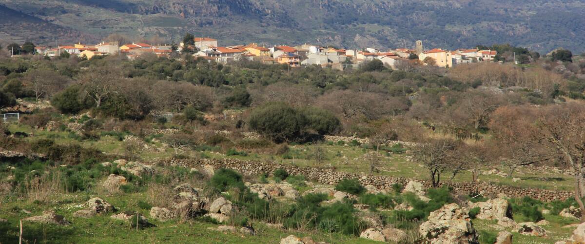 A village with red-roofed houses nestled in a valley with mountains in the background.