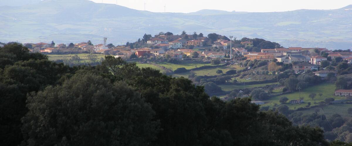 A town nestled in a valley with rolling hills and wind turbines in the distance.