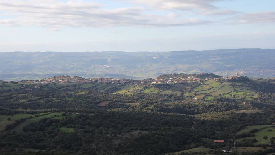 A panoramic view of a hilly landscape with scattered buildings and a distant town.