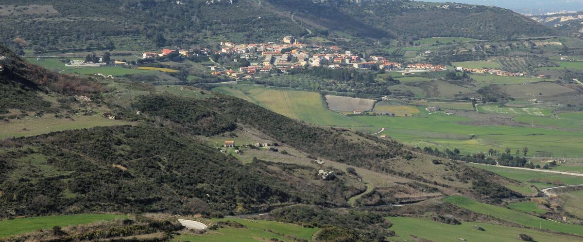 A hilly landscape with a small town nestled among green fields and scattered buildings.