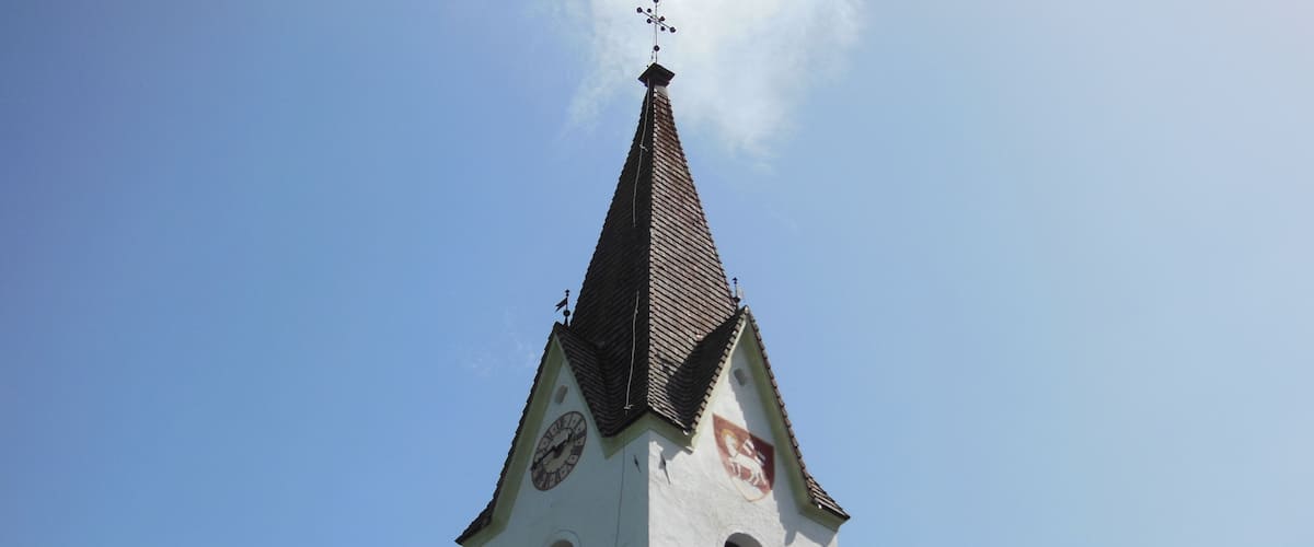A church tower with a clock and a weather vane.