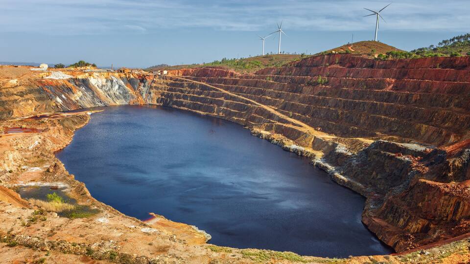 A large open-pit mine with a deep pit and wind turbines in the background.