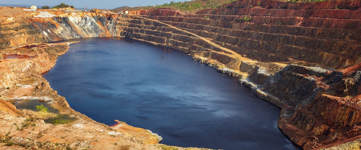 A large open-pit mine with a deep pit and wind turbines in the background.