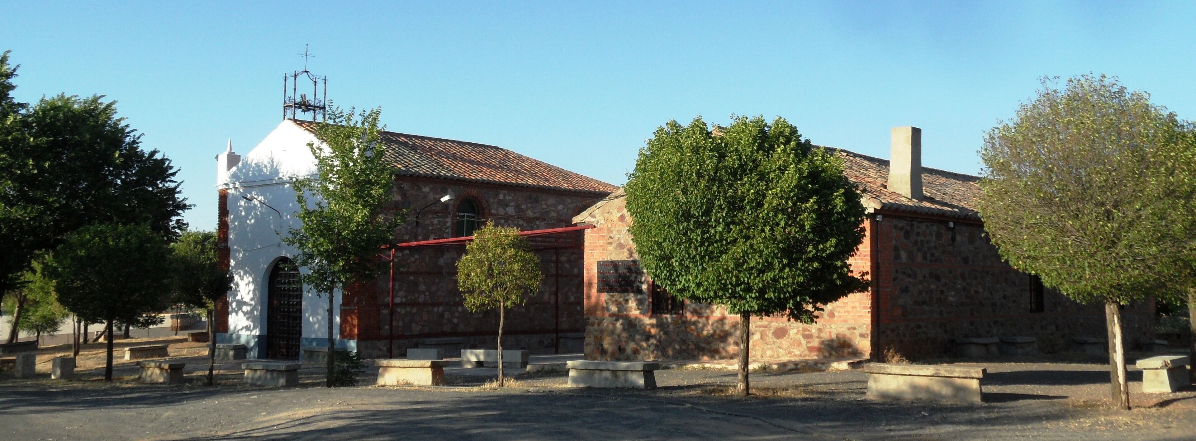 A church with a white facade and a red roof, surrounded by trees and benches.