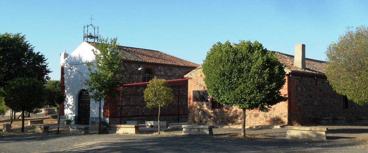A church with a white facade and a red roof, surrounded by trees and benches.