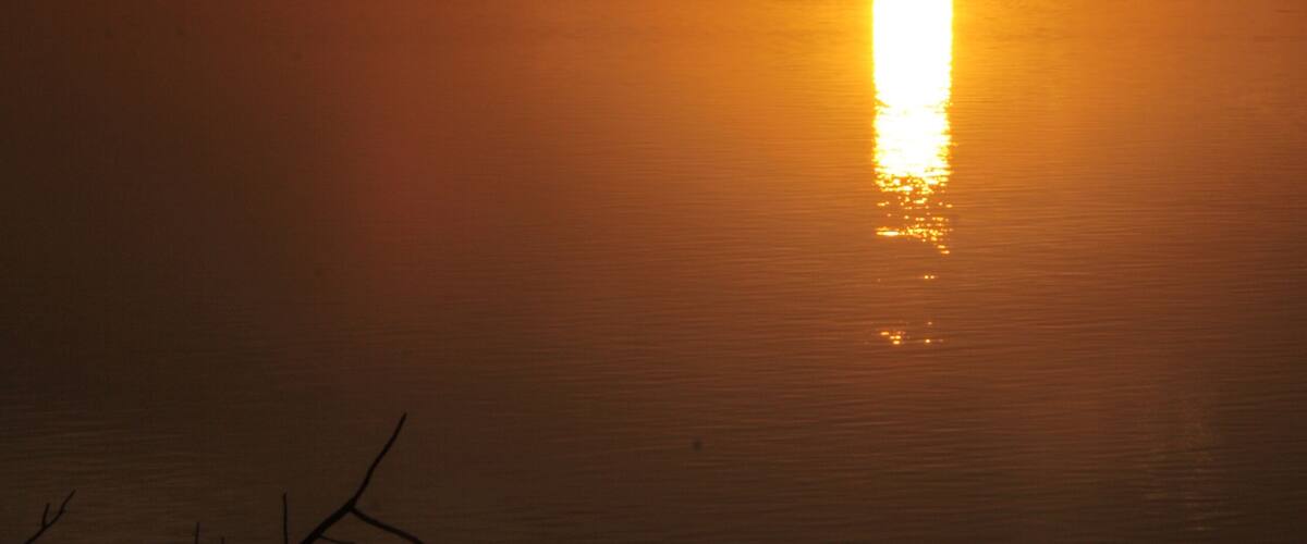 A sunset over a calm lake with a silhouette of trees and a distant horizon.