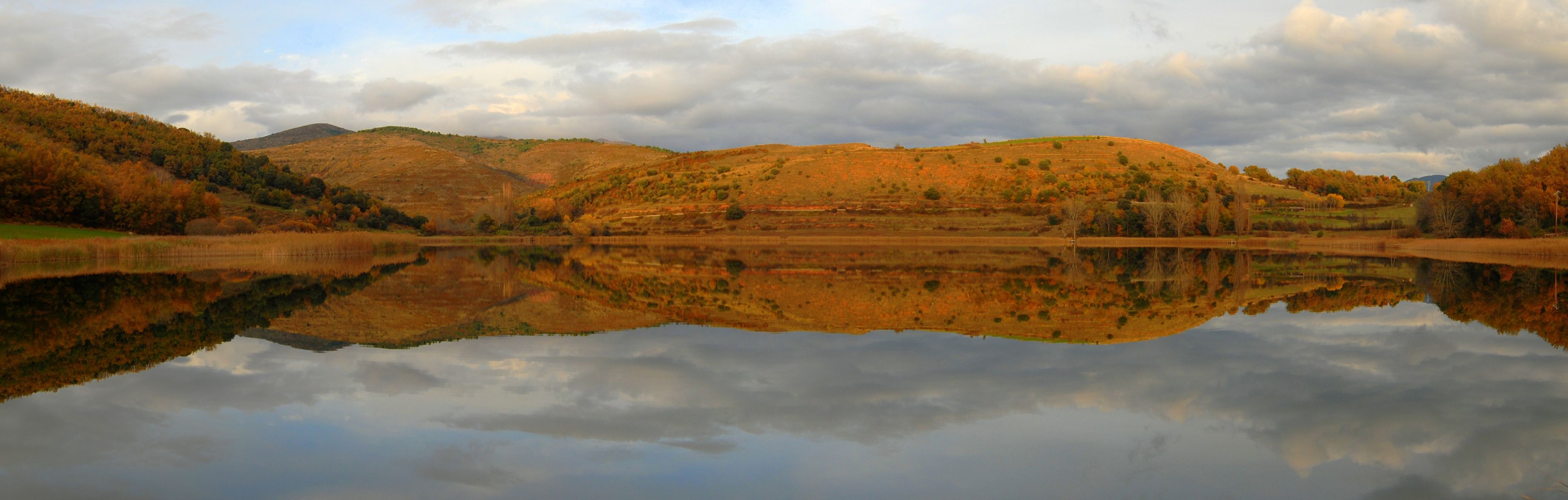 A calm lake reflecting the surrounding hills and trees.