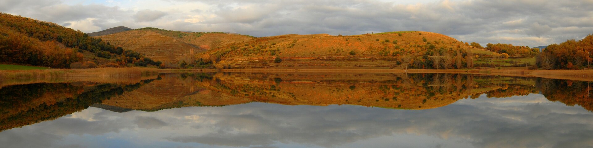 Un lago tranquilo que refleja las colinas y árboles circundantes.