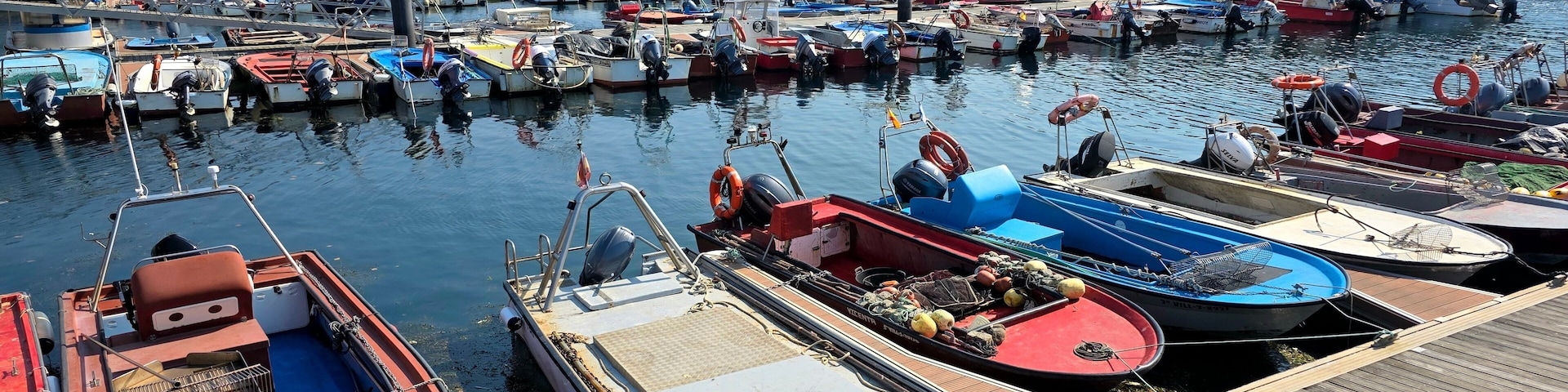 Un puerto con numerosos barcos amarrados, un muelle de madera y edificios al fondo.