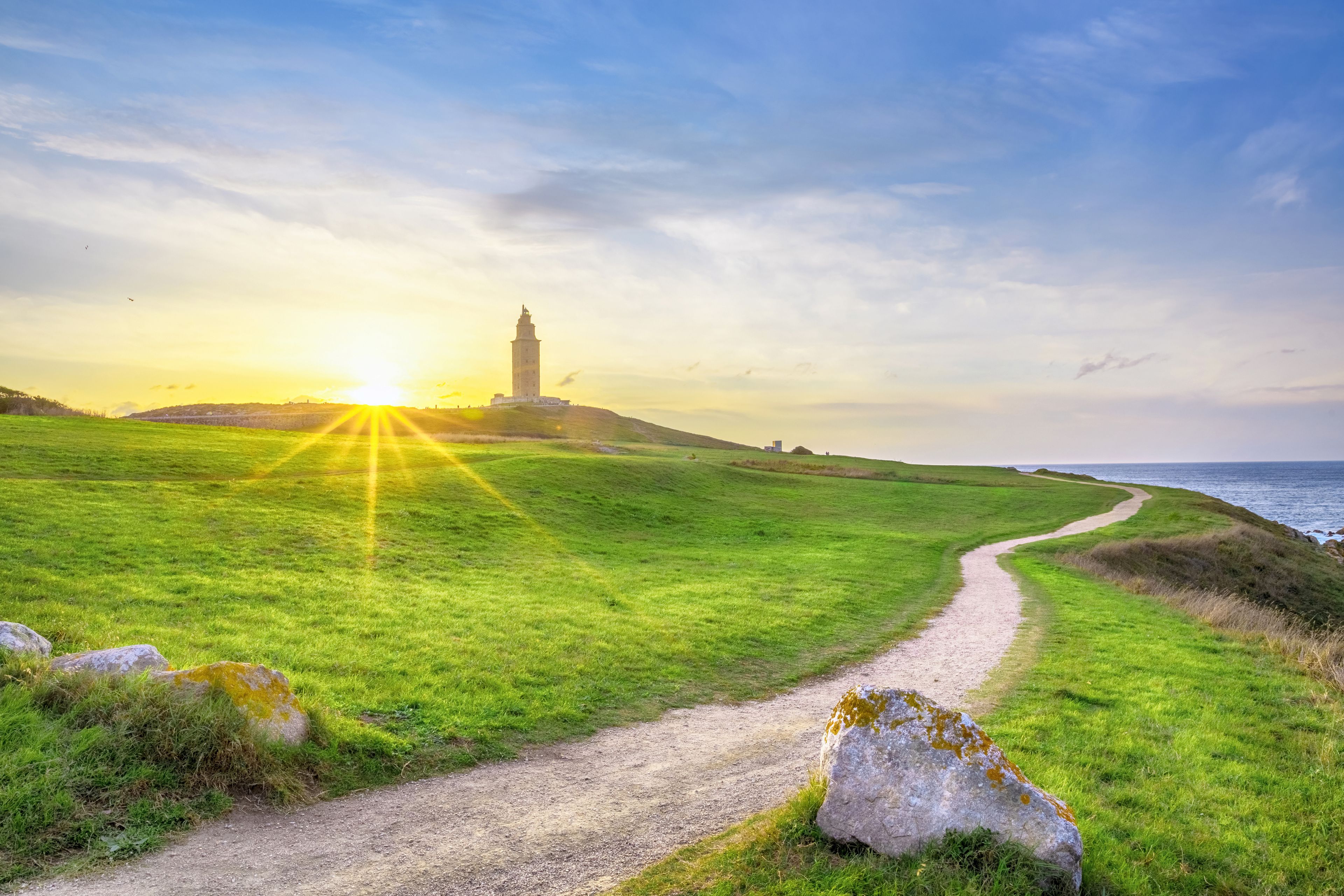 A coastal landscape with a grassy path, a lighthouse, and the ocean in the background.
