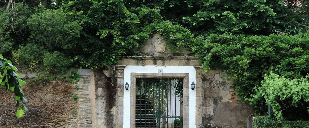 A stone gate with a metal gate, surrounded by lush greenery and a stone wall.