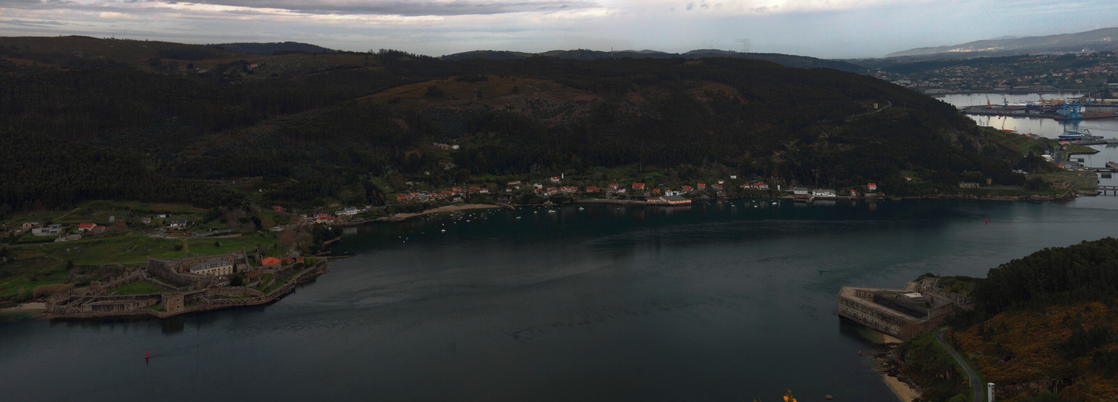A coastal town with a historic fort, a river, and a mountainous backdrop.