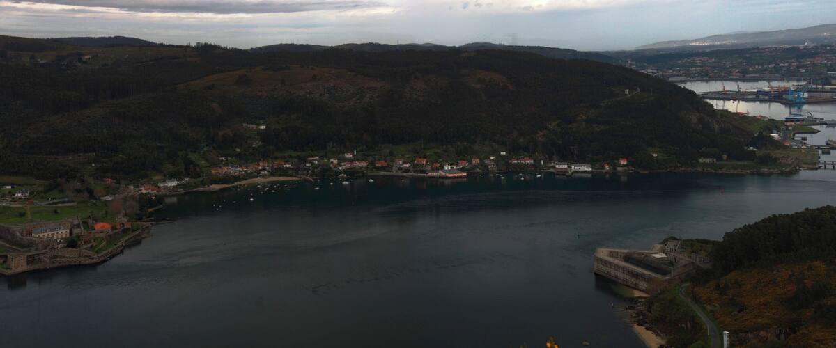A coastal town with a historic fort, a river, and a mountainous backdrop.