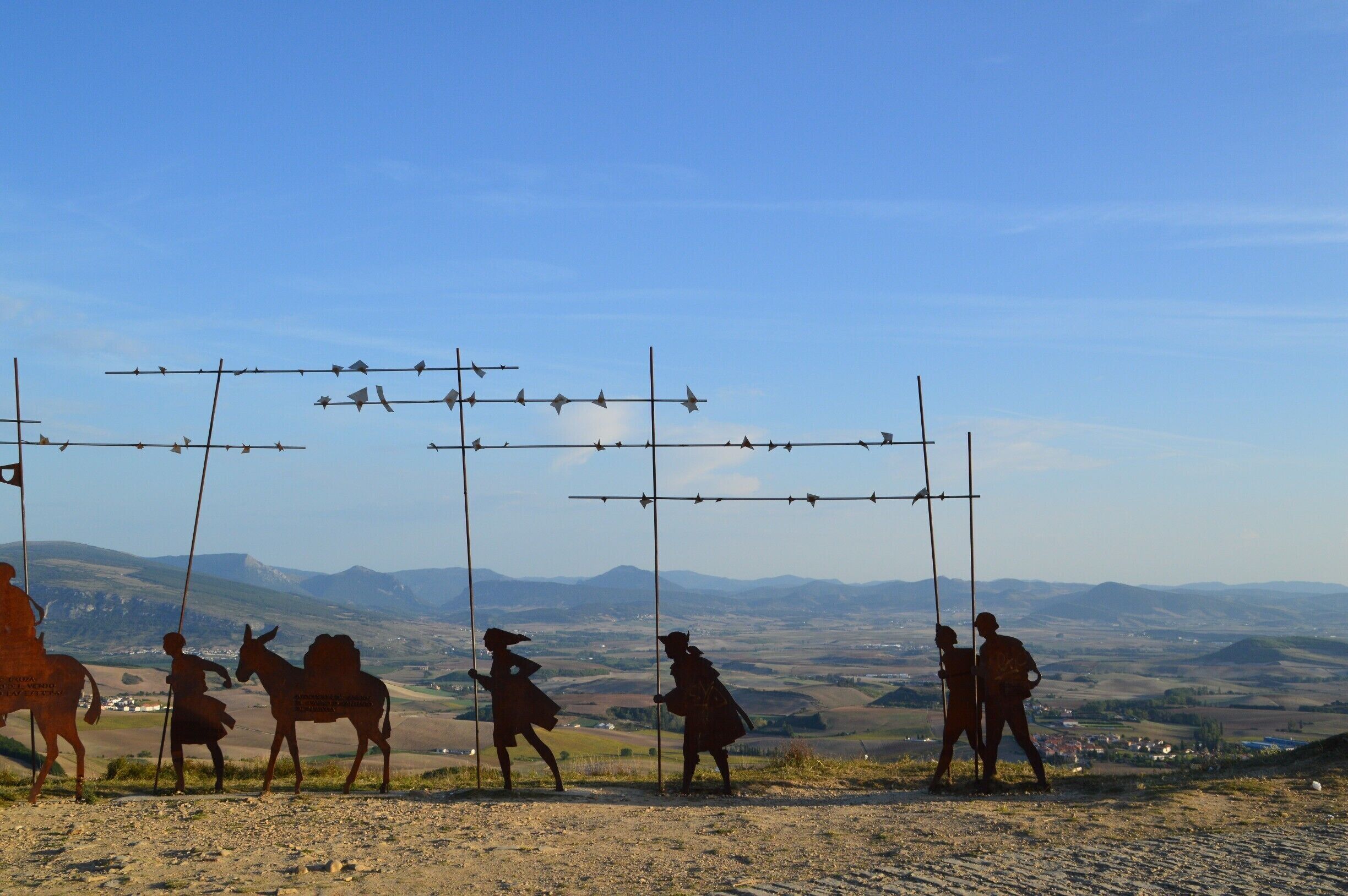A silhouette of people and a donkey on a hill with barbed wire fences in the background.