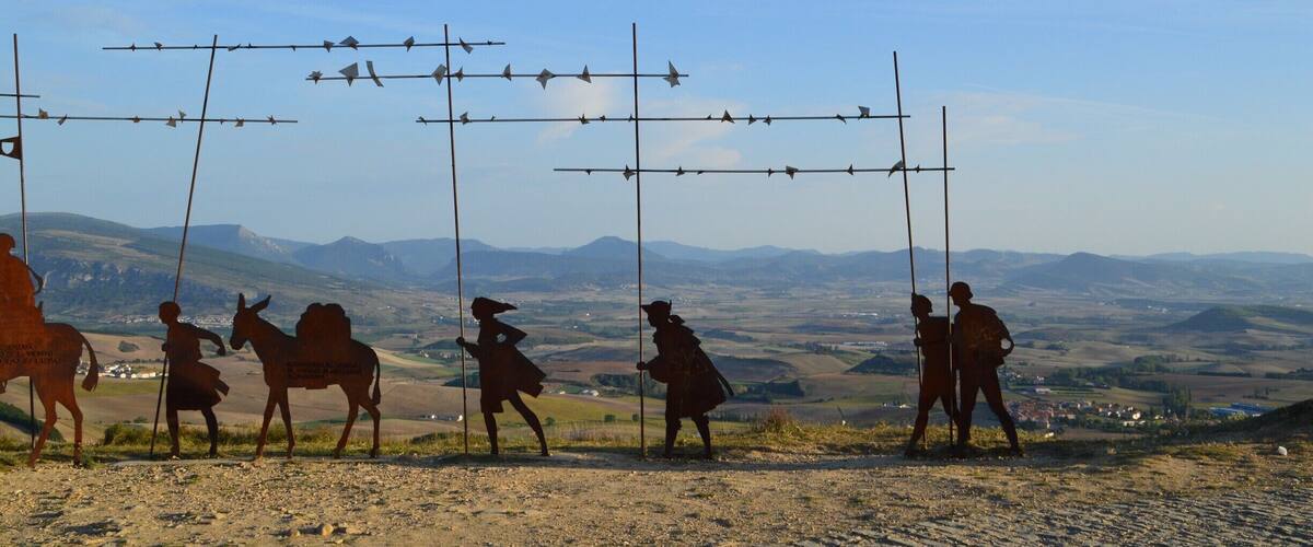 A silhouette of people and a donkey on a hill with barbed wire fences in the background.