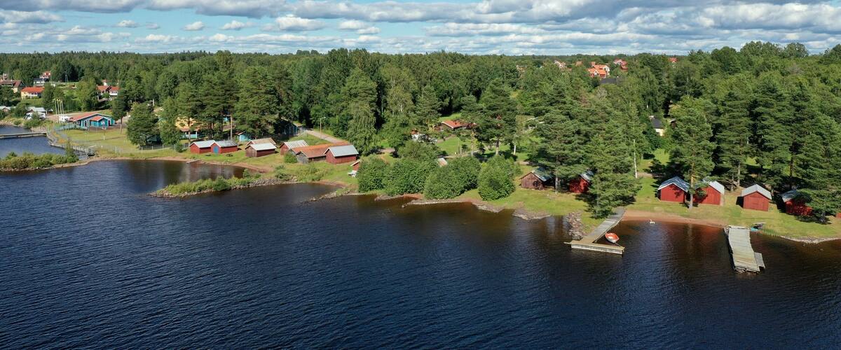 A lakeside community with red-roofed cabins and a dense forest in the background.