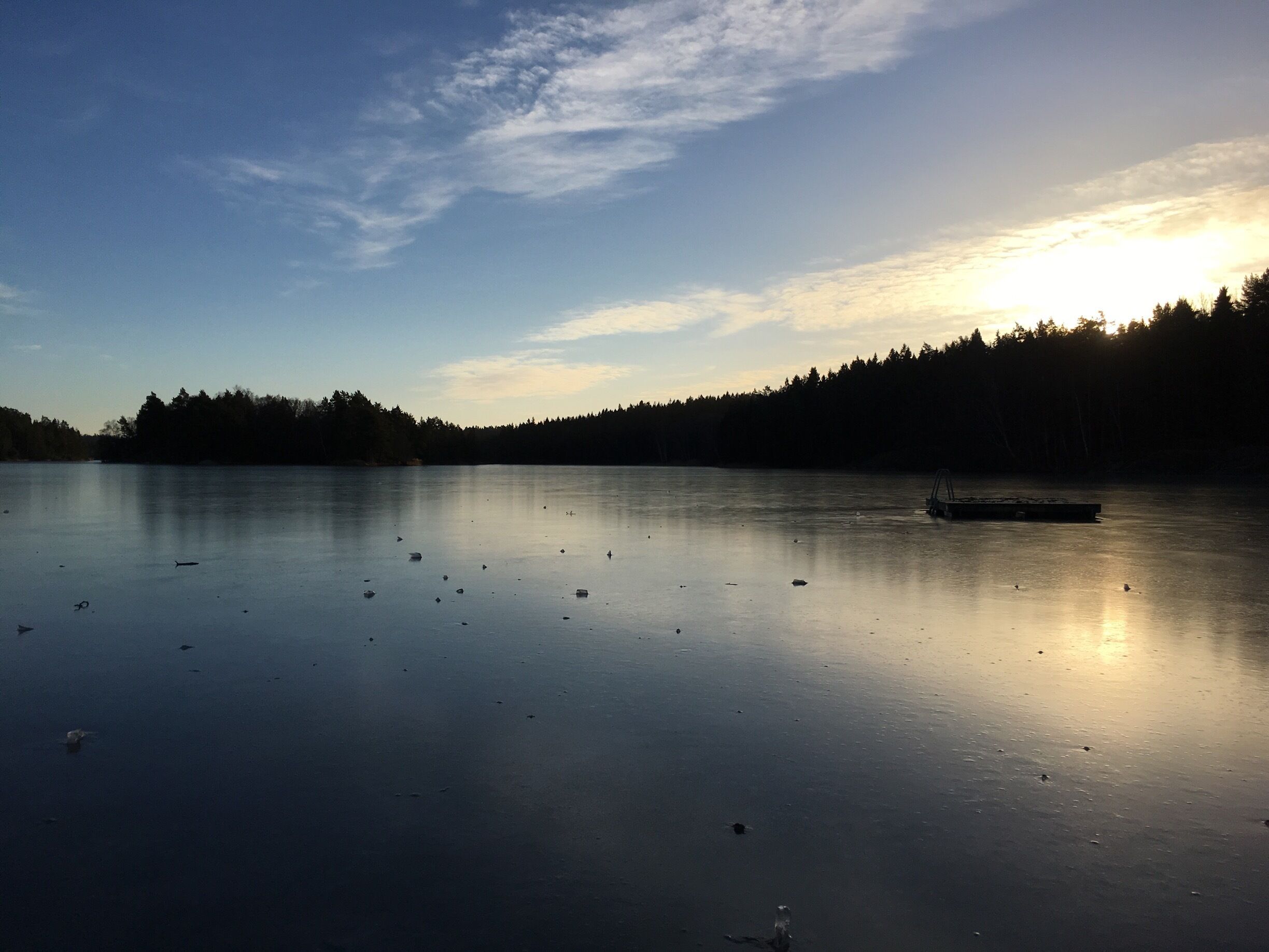 A calm lake with a boat, surrounded by a forested shoreline and a clear sky.