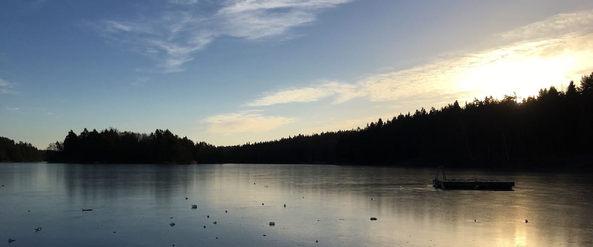 A calm lake with a boat, surrounded by a forested shoreline and a clear sky.