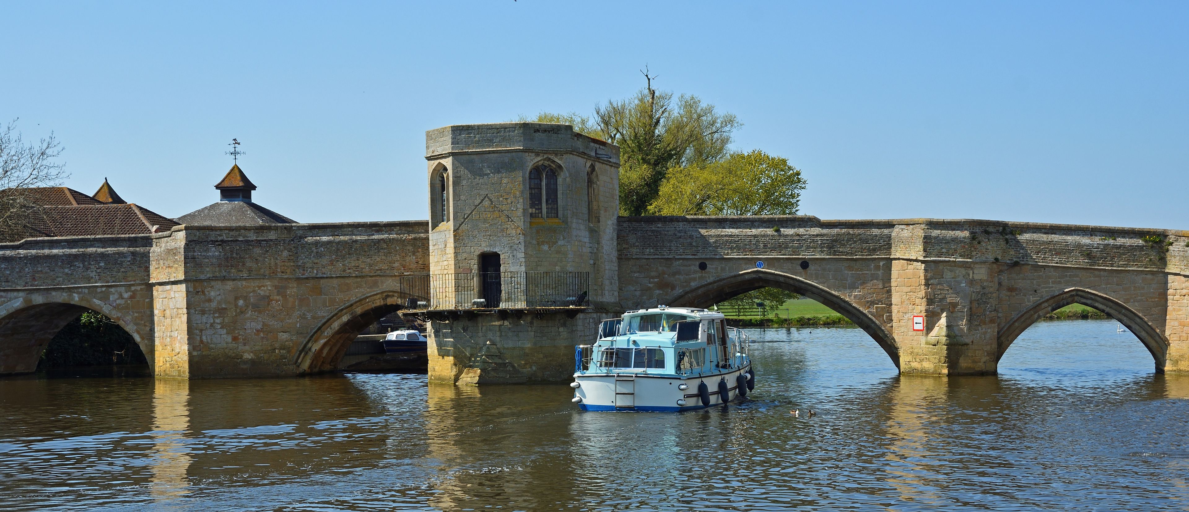 A stone bridge with a tower and a boat on the water.