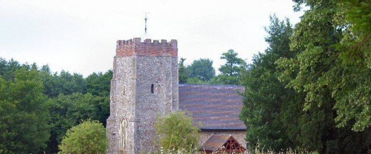 A stone tower with a red roof, surrounded by greenery and a wooden fence.