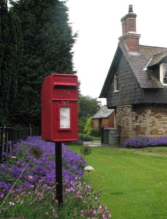 Teigh: postbox E II R postbox on a stick and some bright borders, on a showery afternoon.