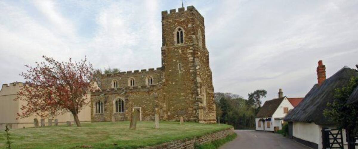 A historic stone church with a tall tower, a paved street, and traditional houses.