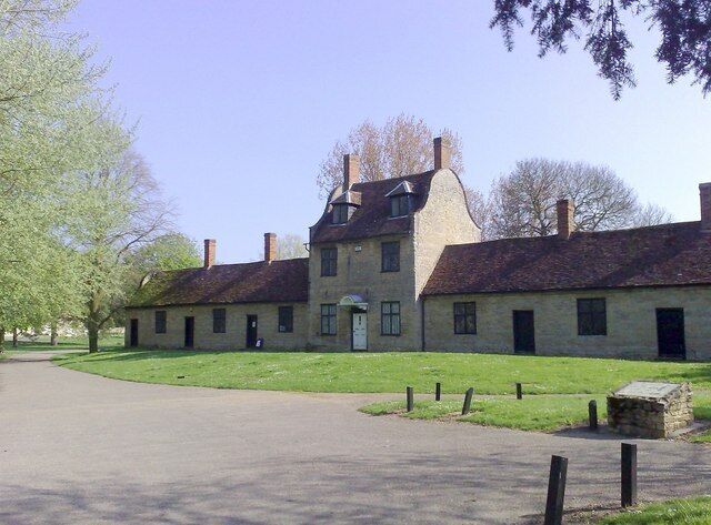 A historic stone building with a central entrance, surrounded by a paved driveway and grassy areas.