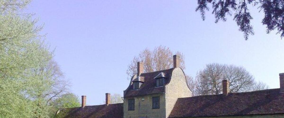 A historic stone building with a central entrance, surrounded by a paved driveway and grassy areas.