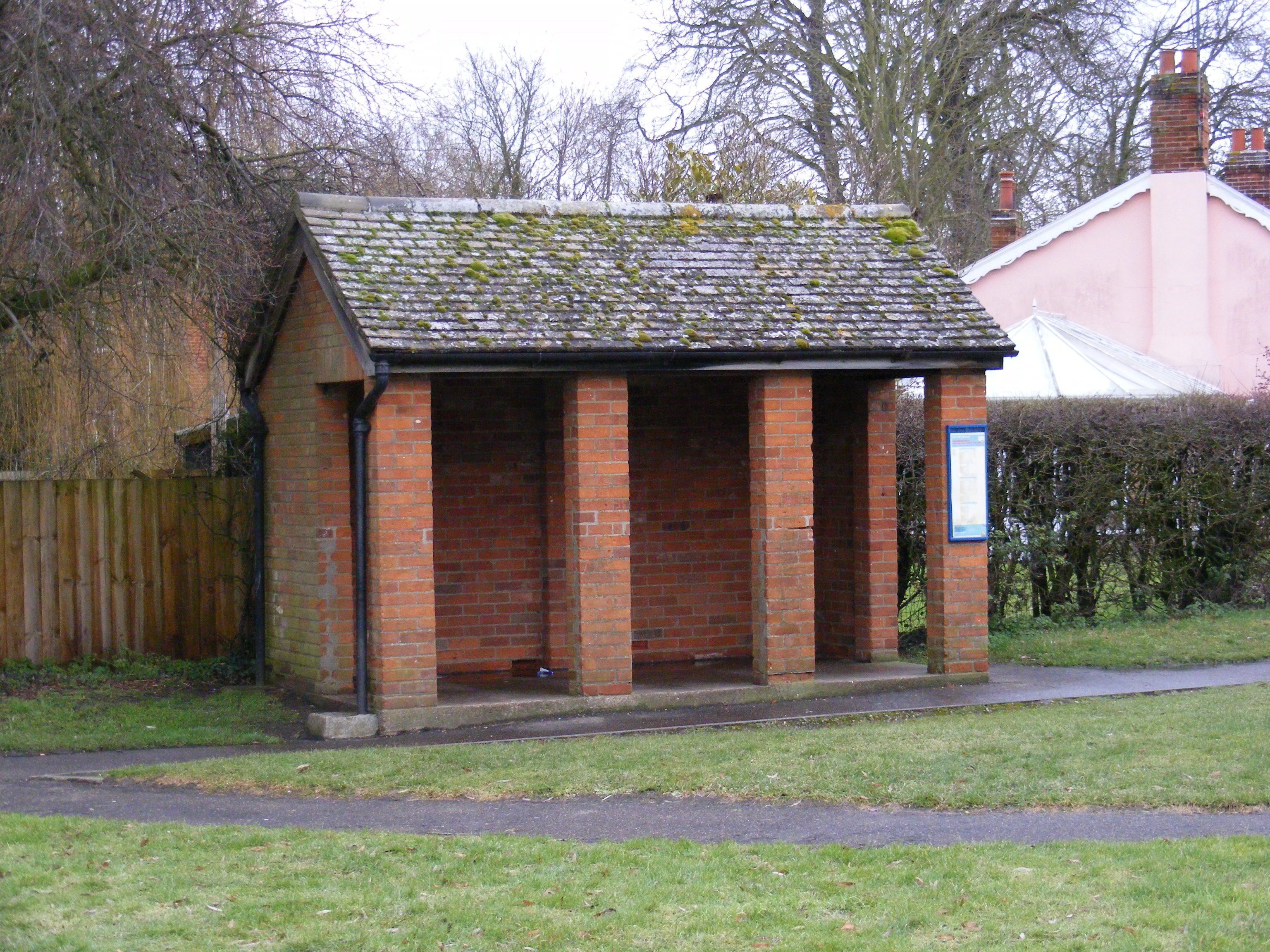 A small brick structure with a tiled roof, surrounded by grass and a wooden fence.