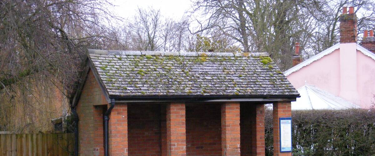 A small brick structure with a tiled roof, surrounded by grass and a wooden fence.