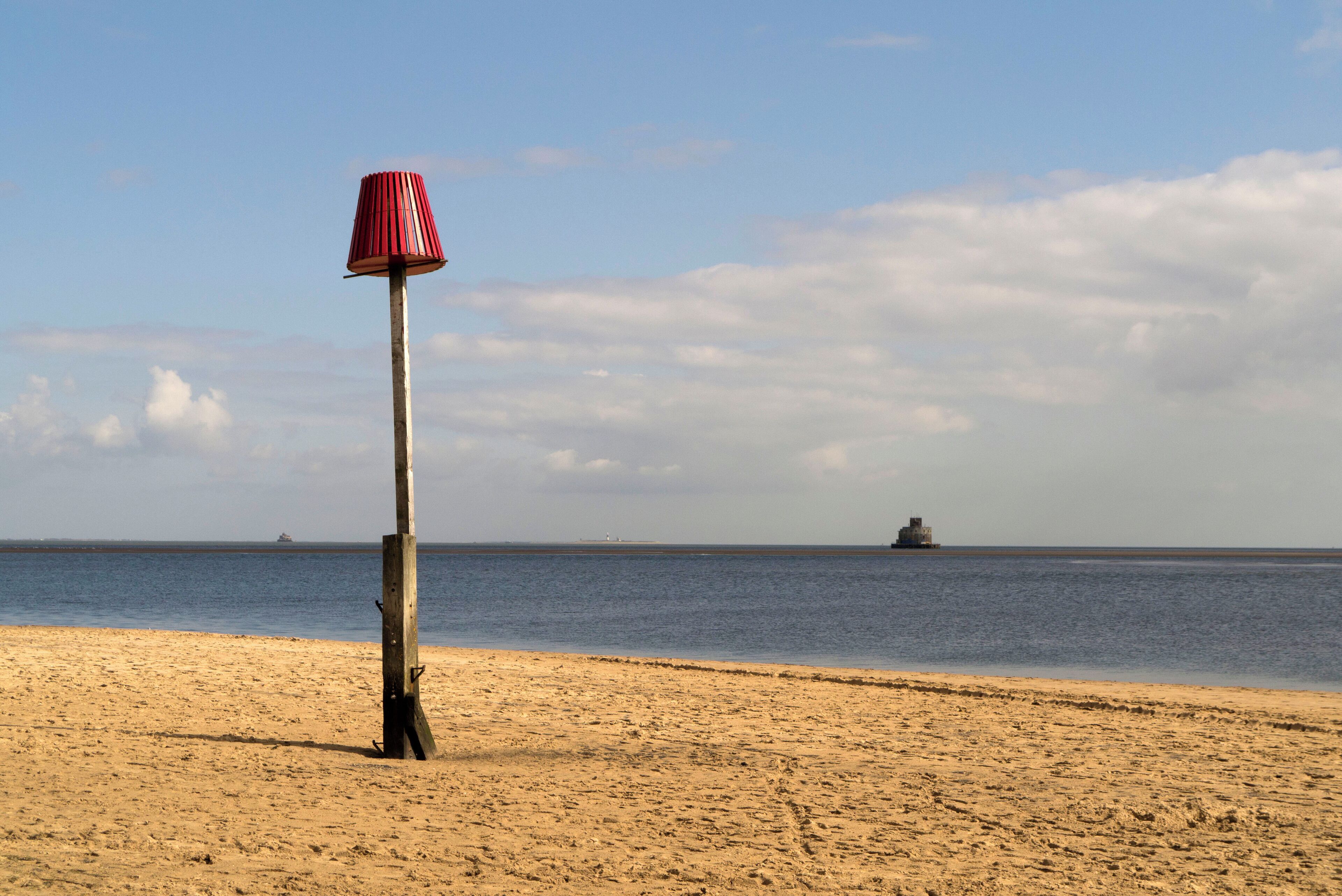 A sandy beach with a red and white striped lamp post and a calm sea in the background.