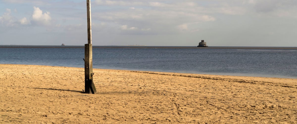 A sandy beach with a red and white striped lamp post and a calm sea in the background.