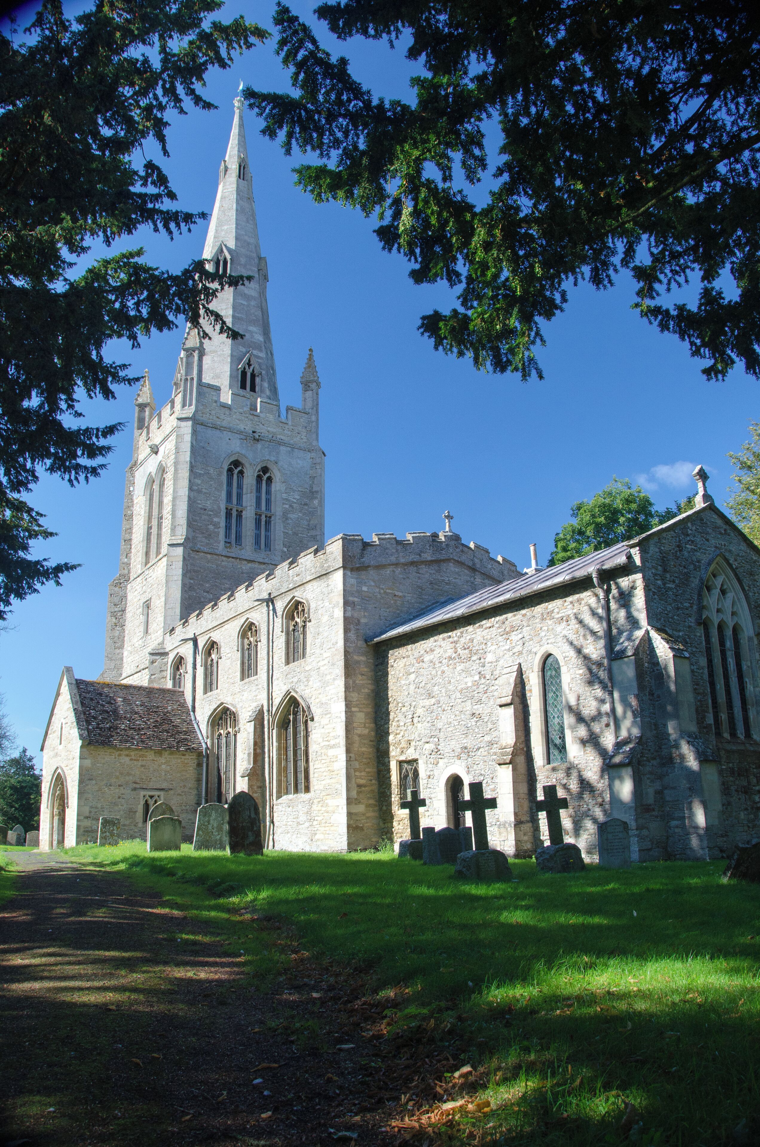 A historic church with a tall spire, stone walls, and a graveyard with headstones.